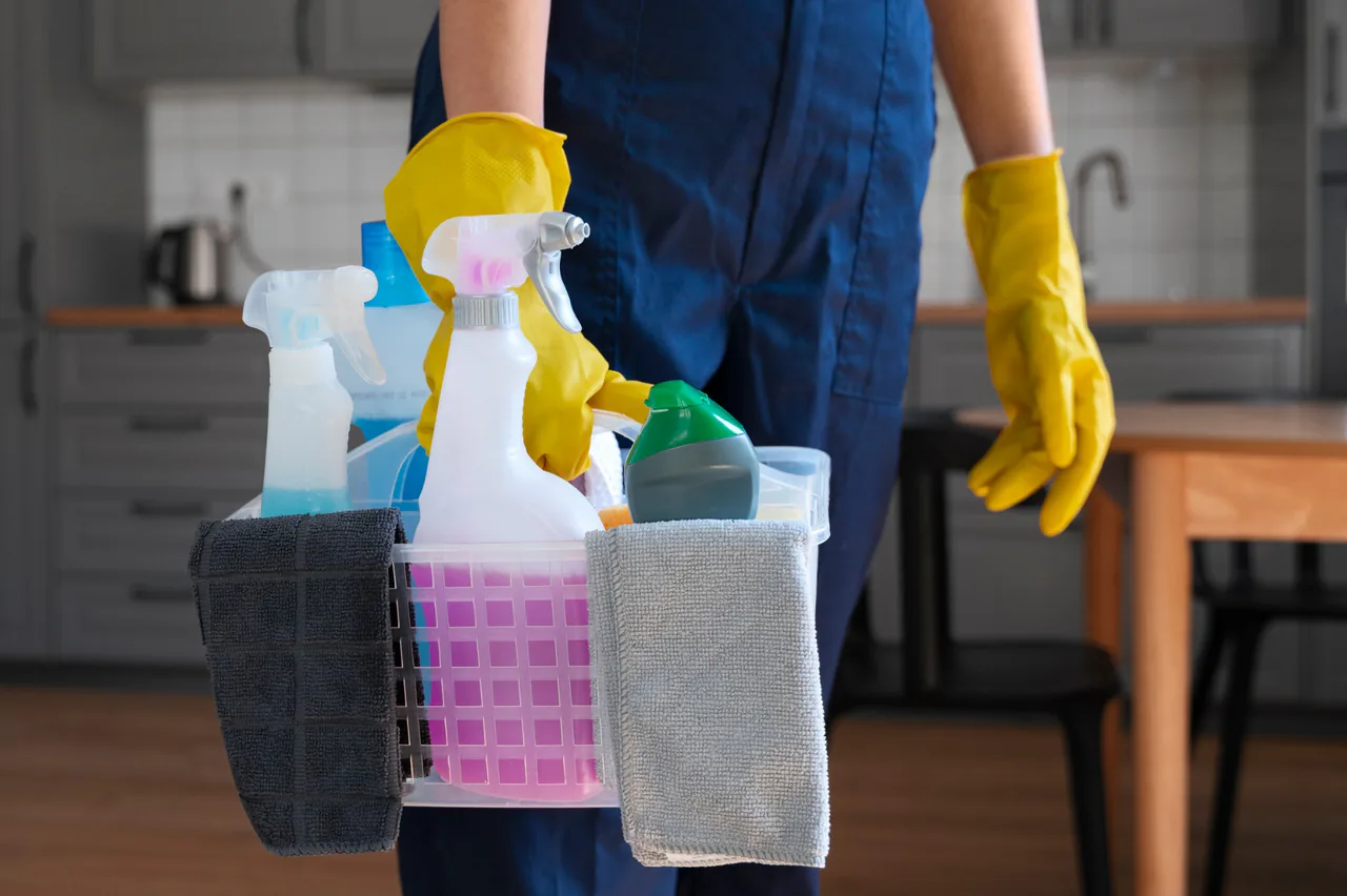 Profissional de luvas amarelas carregando cesto com produtos de limpeza
